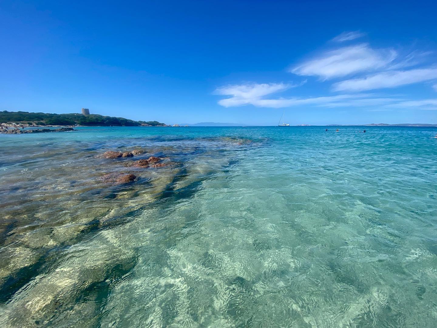 Acqua limpida e scogli a Vignola Mare, con la torre sul promontorio in lontananza
